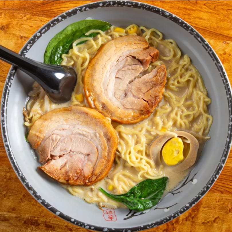Aiki Sushi & Ramen's tonkotsu ramen with pork belly, egg, spinach, and corn in a gray bowl.