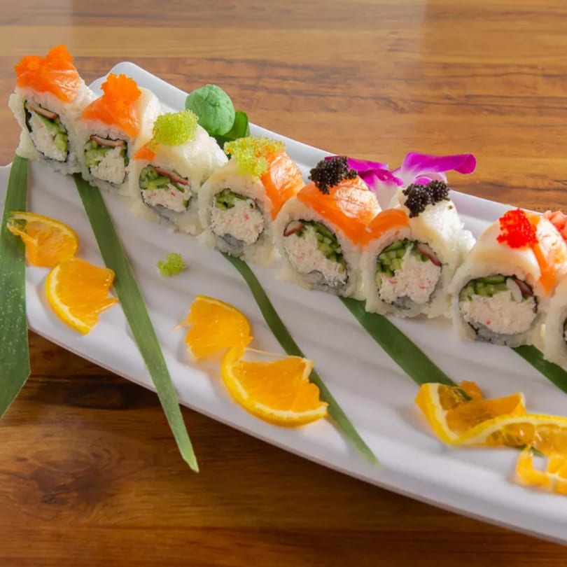 A long white plate of Aiki Sushi & Ramen sushi rolls, garnished with orange slices and green leaves.